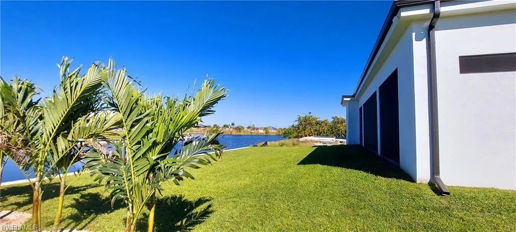 The property features a well-maintained lawn, palm trees, and a clear view of the water under a bright blue sky