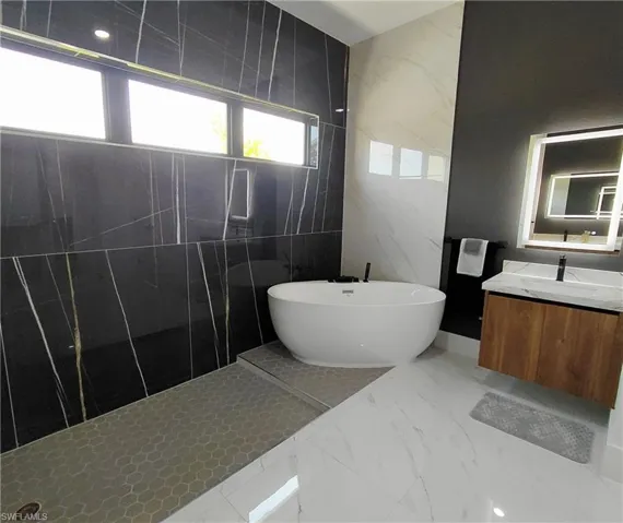 Luxurious bathroom featuring a freestanding soaking tub, large format black and white marbled wall tiles, a floating wood vanity with a marbled countertop, and an illuminated vanity mirror