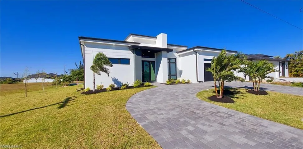The property features a modern exterior with a white facade, a dark gray paved driveway, and a well-maintained lawn