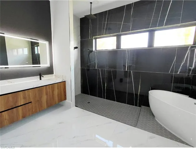 Luxurious bathroom featuring a floating vanity with a marble-patterned countertop, a sleek illuminated mirror, a spacious walk-in shower with black marble-patterned tiling, and a freestanding soaking tub