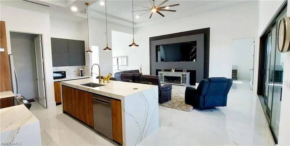 Open concept living area featuring a modern kitchen island with an integrated sink and dishwasher, white countertops, and a living room with a feature wall and television