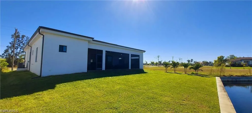 The property features a white exterior, a well-maintained green lawn, and a paved canal edge