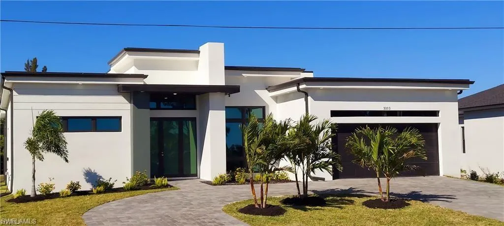 The property features a modern exterior with a white facade and dark accents, a paver driveway, and a well-maintained lawn with landscaping