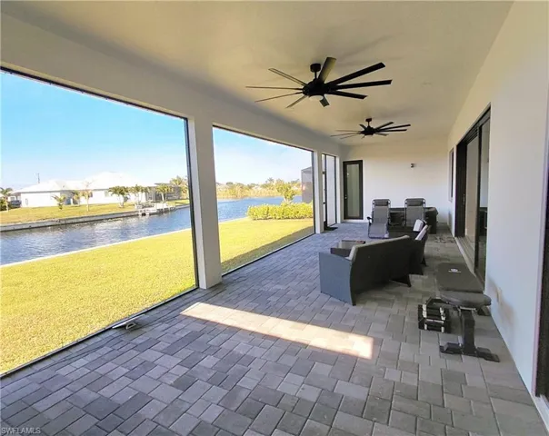 Expansive outdoor living area featuring a paved patio, ceiling fans, and a scenic view of the canal and lush green lawn