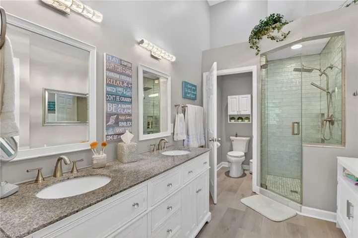 double vanity, a shower stall, and light wood-style flooring