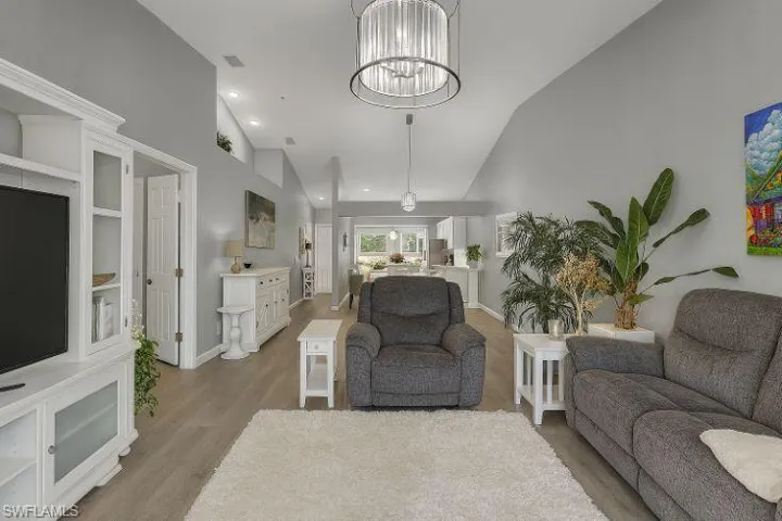 Living area with light wood-style floors, lofted ceiling, and suspended lighting