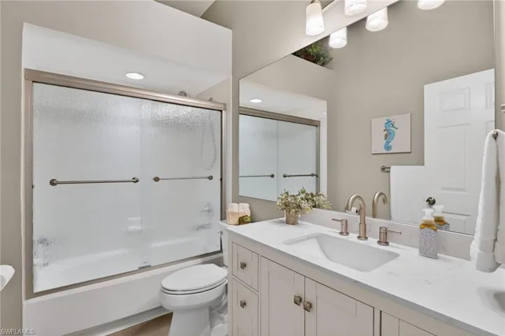 Bathroom featuring double vanity and bath / shower combo with glass door