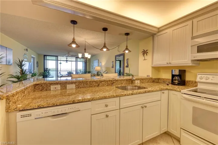 Kitchen with white appliances, light stone counters, hanging light fixtures, a peninsula, and a textured ceiling
