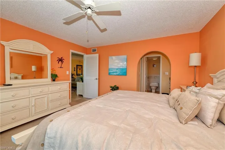 Bedroom featuring light colored carpet, ceiling fan, a textured ceiling, arched walkways, and connected bathroom