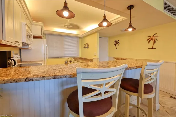 Kitchen with a tray ceiling, light stone countertops, wainscoting, a peninsula, and decorative light fixtures