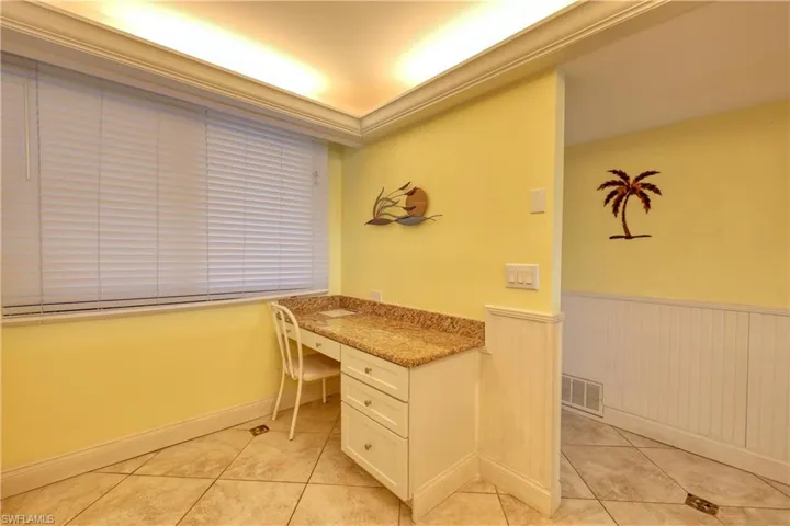 Unfurnished office featuring built in desk, a wainscoted wall, ornamental molding, and light tile patterned floors