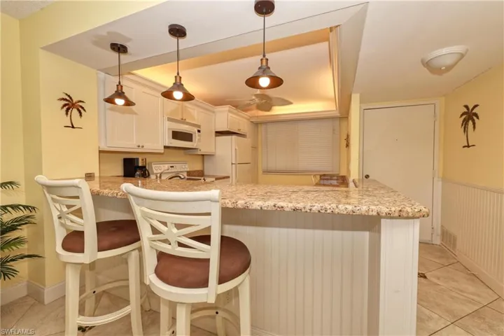 Kitchen with a peninsula, light tile patterned flooring, light stone counters, a breakfast bar area, and hanging light fixtures