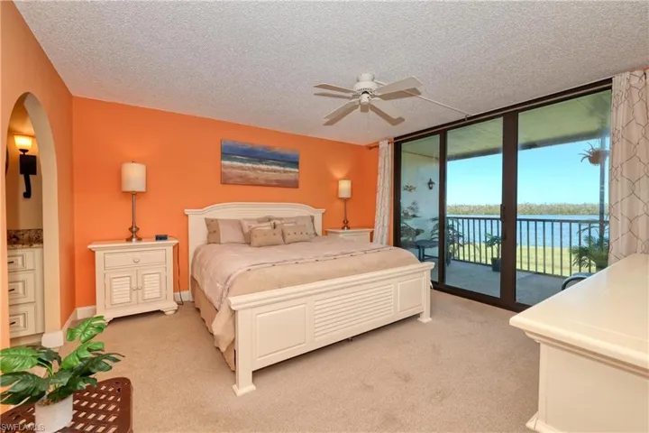 Bedroom featuring a wall of windows, light carpet, a water view, access to exterior, and ceiling fan