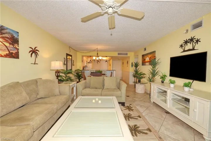 Living room with a textured ceiling, light tile patterned floors, a chandelier, and ceiling fan