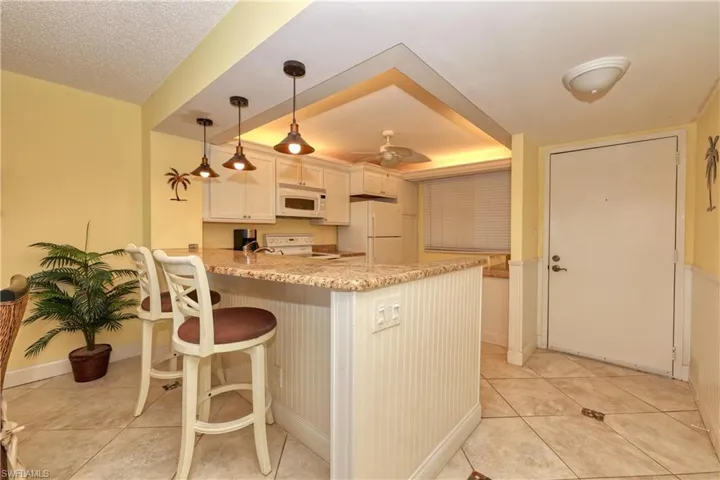 Kitchen featuring a kitchen bar, a peninsula, hanging light fixtures, light stone countertops, and light tile patterned flooring