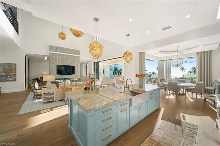 Kitchen with light stone counters, hanging light fixtures, dark wood-style floors, open floor plan, and an island with sink