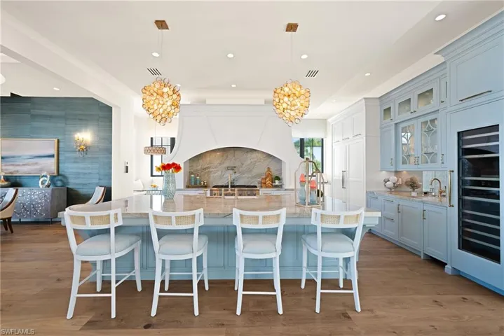 Kitchen with hanging light fixtures, light stone countertops, a large island, tasteful backsplash, and wine cooler