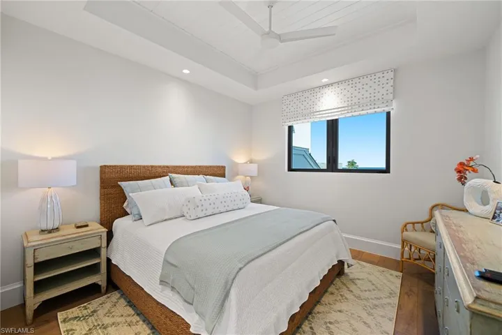Bedroom with a raised ceiling, wood finished floors, and ceiling fan