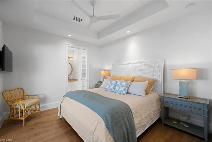 Bedroom featuring a raised ceiling, wood finished floors, ensuite bath, recessed lighting, and a ceiling fan