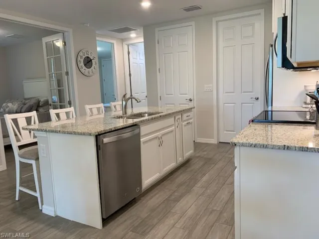 Kitchen featuring sink, white cabinetry, an island with sink, and stainless steel dishwasher