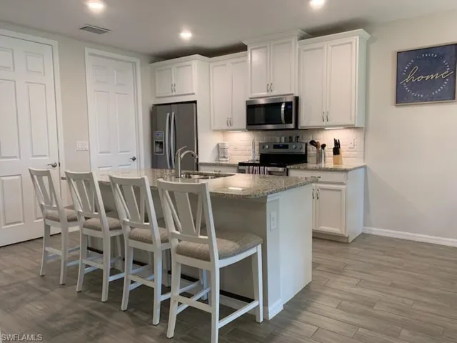 Kitchen with light stone countertops, stainless steel appliances, white cabinets, and a kitchen island with sink