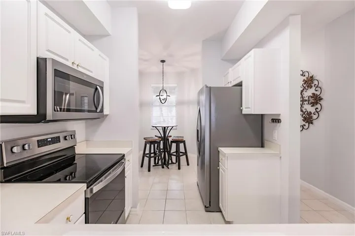 Kitchen featuring hanging light fixtures, appliances with stainless steel finishes, white cabinetry, and light tile flooring