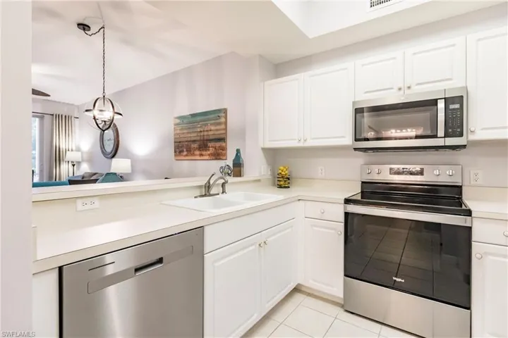 Kitchen with appliances with stainless steel finishes, white cabinetry, sink, and hanging light fixtures