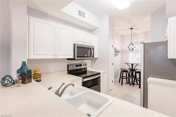 Kitchen featuring light tile flooring, hanging light fixtures, white cabinetry, appliances with stainless steel finishes, and sink