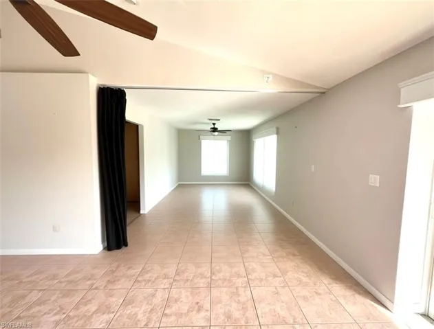 Empty room with a ceiling fan, vaulted ceiling, and light tile patterned floors