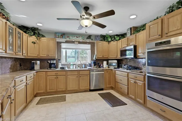 Kitchen featuring stainless steel appliances, a ceiling fan, glass fronted cabinets, light wood finish cabinets, and recessed lighting