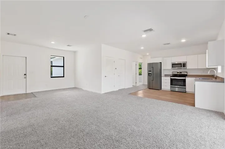 Kitchen with a sink, white cabinets, visible vents, appliances with stainless steel finishes, and light carpet