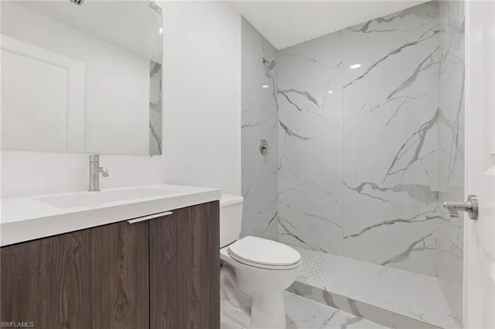 Full bathroom featuring toilet, a marble finish shower, marble finish floor, and vanity