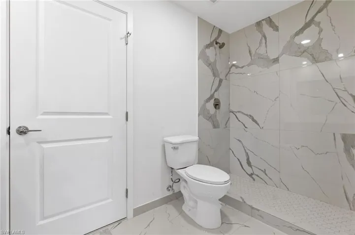 Full bath with a marble finish shower, marble finish floor, baseboards, and toilet