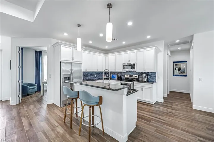 Kitchen featuring stainless steel appliances, tasteful backsplash, white cabinetry, and a kitchen island with sink