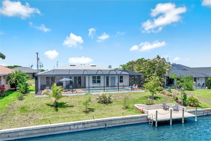 Back of property with a water view, a patio area, an outdoor pool, and a lawn