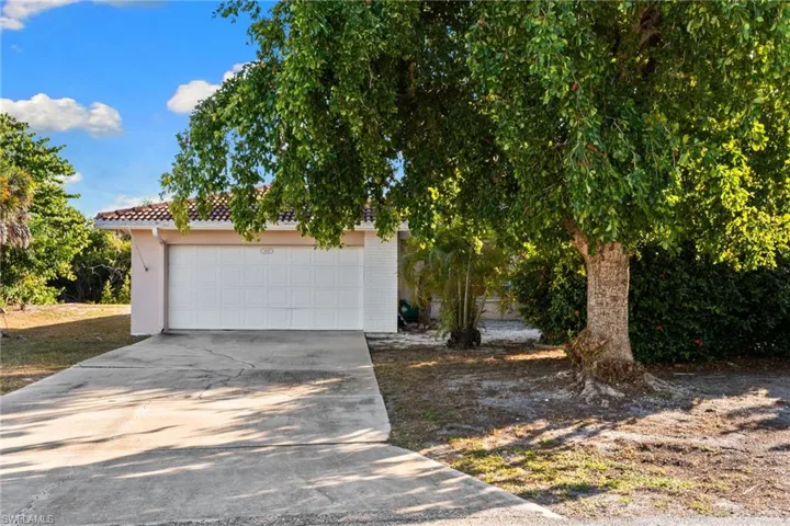 View of property hidden behind natural elements with a garage, a tile roof, driveway, and brick siding