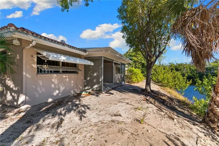 View of side of property with a water view, stucco siding, a tiled roof, and a sunroom