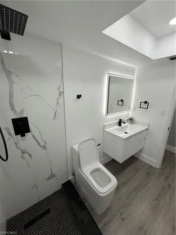 Bathroom with a marble finish shower, wood finished floors, and vanity