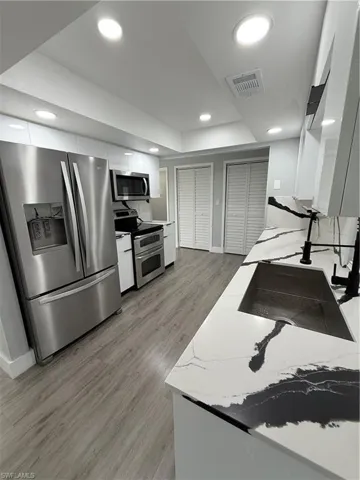 Kitchen featuring refrigerator, range, white cabinets, light wood-type flooring, and recessed lighting