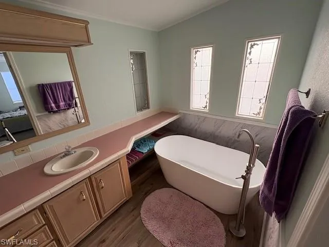 Ensuite bathroom with vanity, a freestanding tub, crown molding, lofted ceiling, and wood finished floors