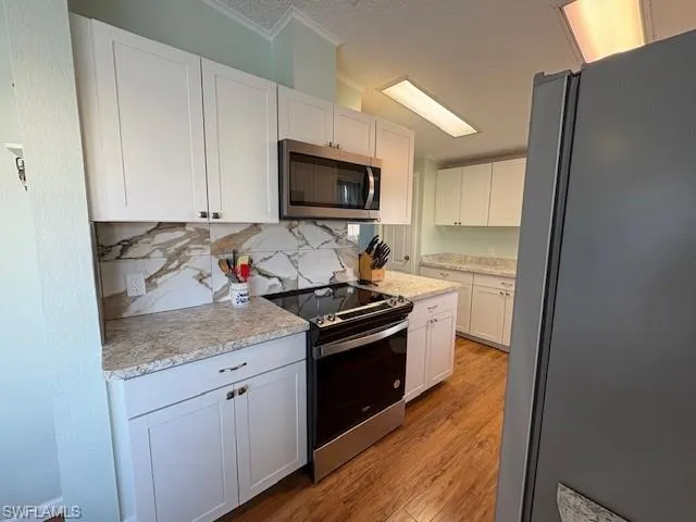 Kitchen with light wood finished floors, white cabinetry, tasteful backsplash, a textured ceiling, and stainless steel appliances