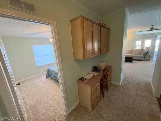 Hallway featuring crown molding, light colored carpet, baseboards, a textured ceiling, and visible vents