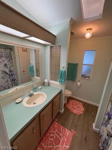 Bathroom featuring crown molding, toilet, vanity, wood finished floors, and baseboards