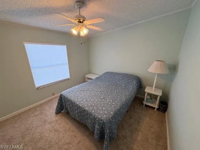 Carpeted bedroom featuring baseboards, crown molding, ceiling fan, and a textured ceiling