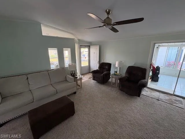 Living area featuring lofted ceiling, ornamental molding, a ceiling fan, and carpet