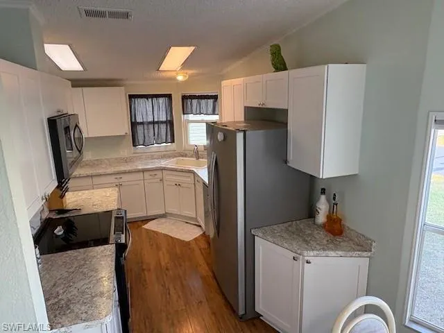 Kitchen with dark wood-type flooring, a sink, visible vents, white cabinets, and appliances with stainless steel finishes