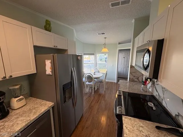 Kitchen featuring a textured ceiling, white cabinets, visible vents, appliances with stainless steel finishes, and dark wood-type flooring