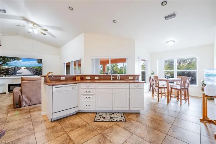 Kitchen with lofted ceiling, white dishwasher, a sink, white cabinets, and open floor plan