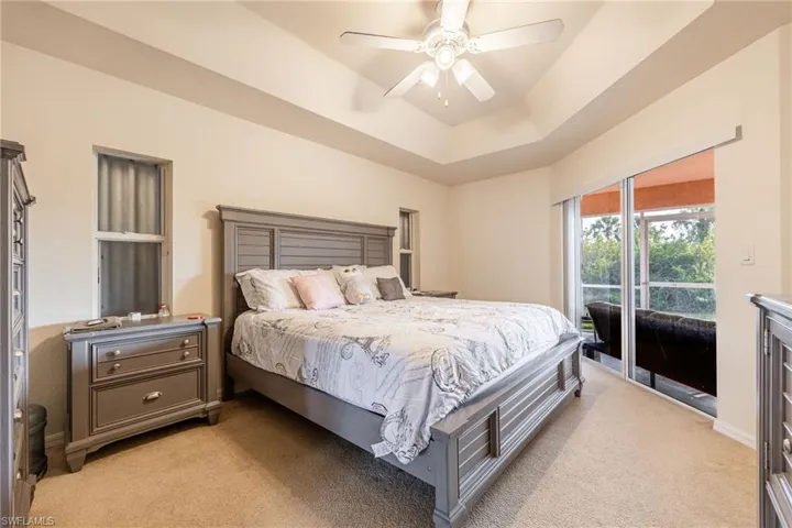 Bedroom with light carpet, access to outside, a tray ceiling, and a ceiling fan