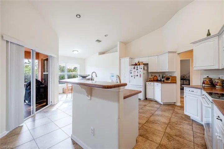 Kitchen with visible vents, a kitchen island with sink, white cabinetry, high vaulted ceiling, and white appliances